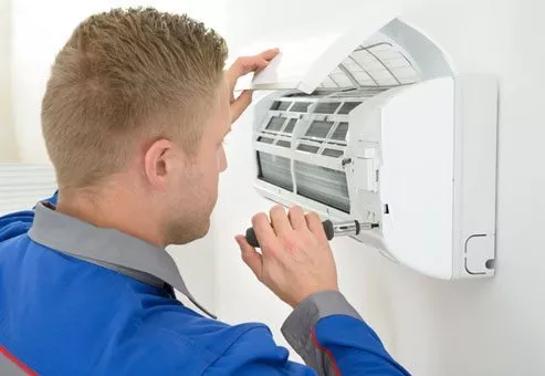HVAC technician repairing a ductless mini-split on a white wall.