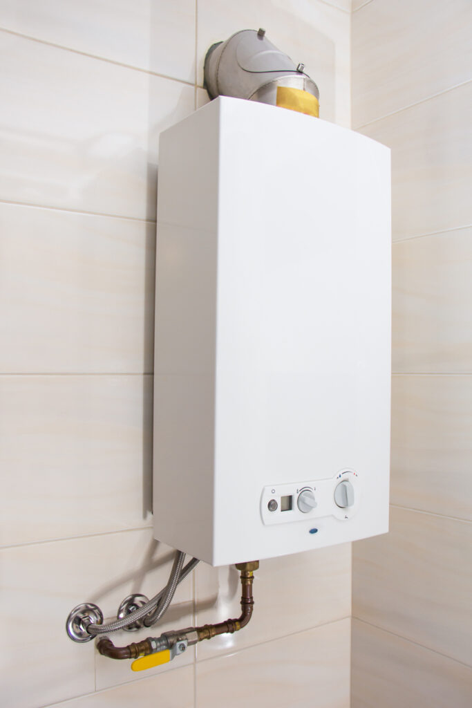 White tankless water heater mounted to white tile wall in bathroom.