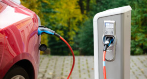 Close-up of a red electric car plugged into an EV charging station in a driveway. 